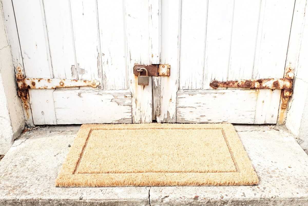 A new welcome mat in front of a rusted door