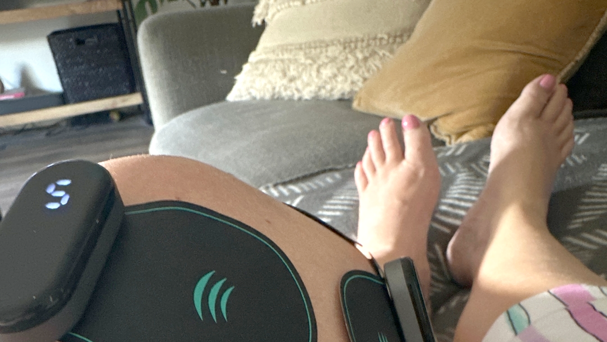 A real customer resting on her couch, feet up, with Vibit PULSE units and pads on her knee